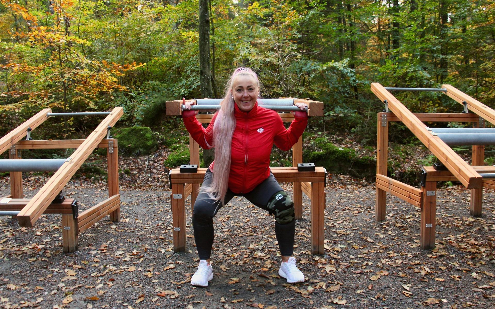 Carina Lindström visar squats, även kallade knäböj, med fokus på rumpan. Man placerar stången på skuldrorna och med stolt hållning böjer man på benen.